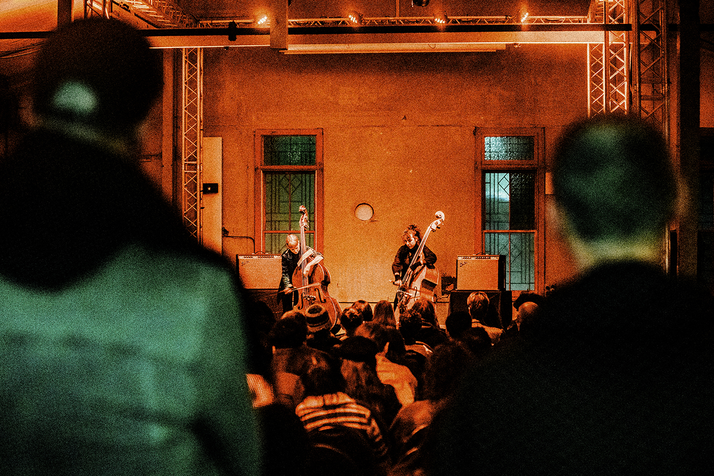 Two musicians photographed over the shoulders of audience members playing contrabas on stage